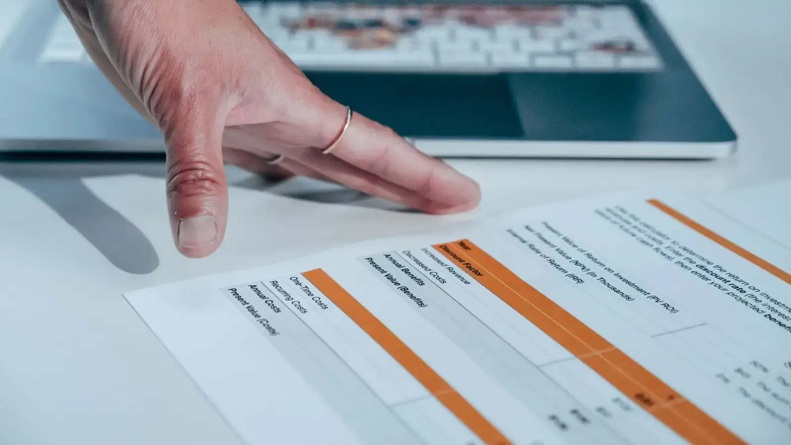A hand resting on a printed financial report in front of a laptop