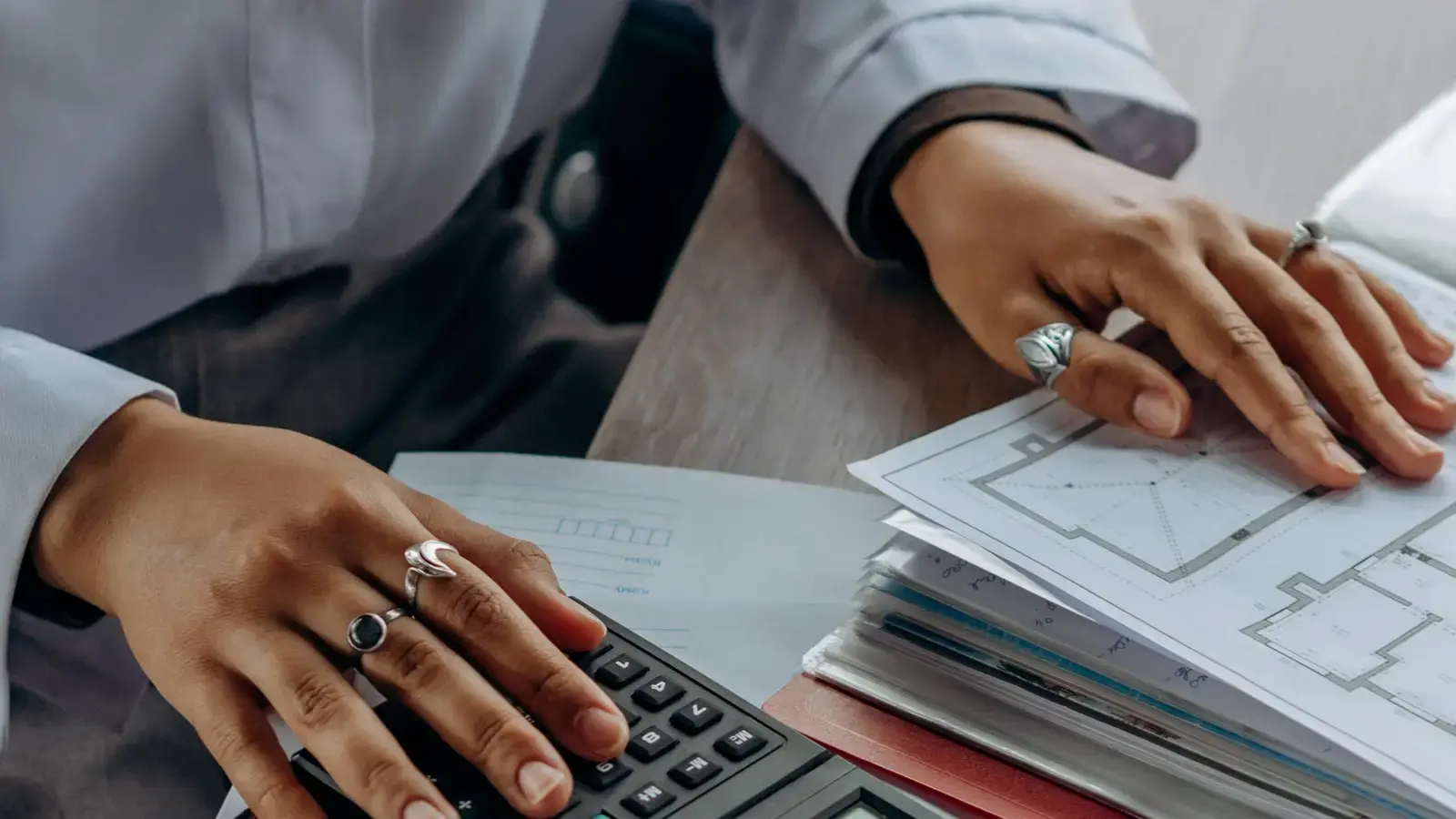 Hands using a calculator beside a stack of documents